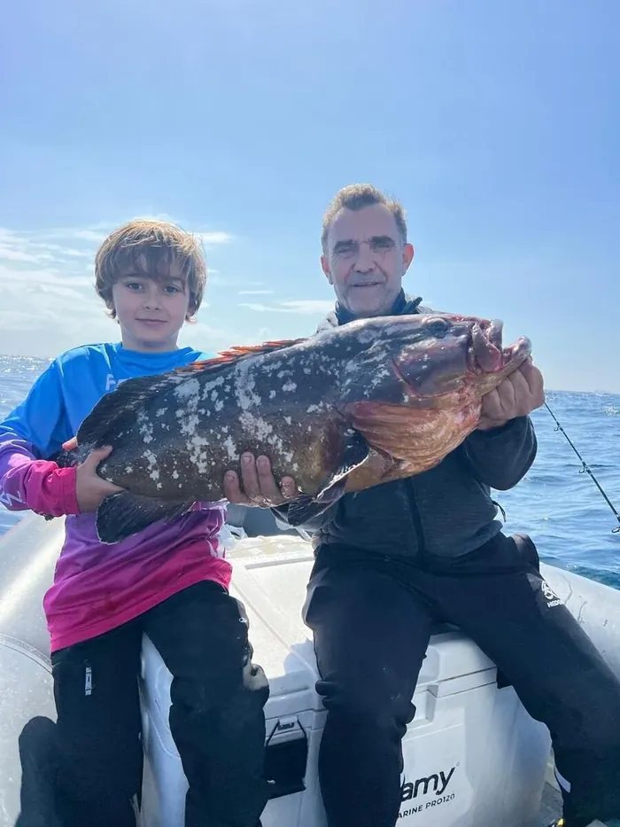 Grandfather and grandson holding a grouper caught during a fishing trip in Marbella