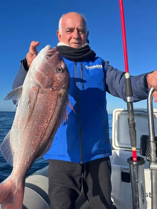 Angler in a blue jacket holding a fish caught next to a bent rod during a fishing trip in Marbella
