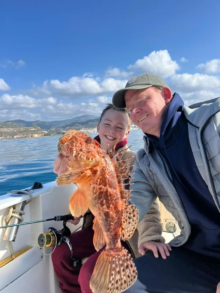 Father and son showing a scorpionfish caught during a family fishing trip in Marbella