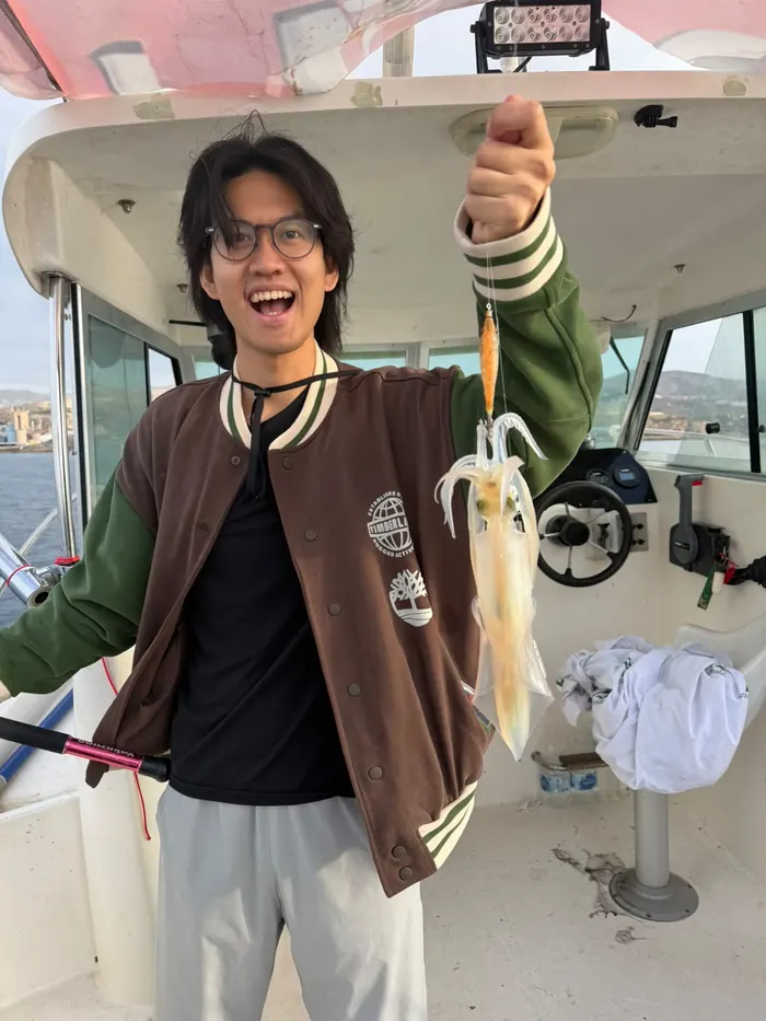 Smiling young man holding up a freshly caught squid on board during a squid fishing trip in Marbella